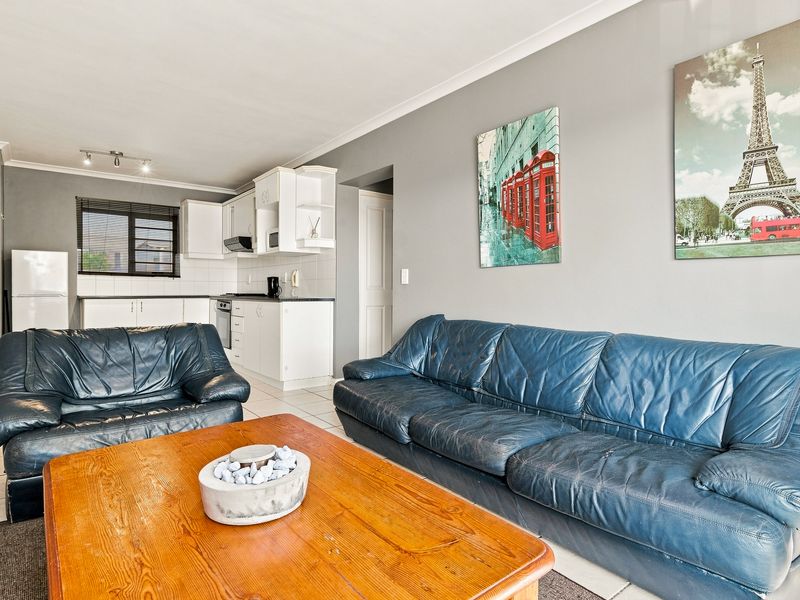 Open-plan living area featuring a functional kitchen with built-in cabinetry, oven, and extractor fan, seamlessly connected to the lounge space with tiled flooring.