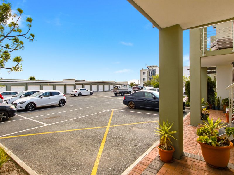 View of the apartment complex parking area featuring paved bays, a covered walkway, and structural columns.