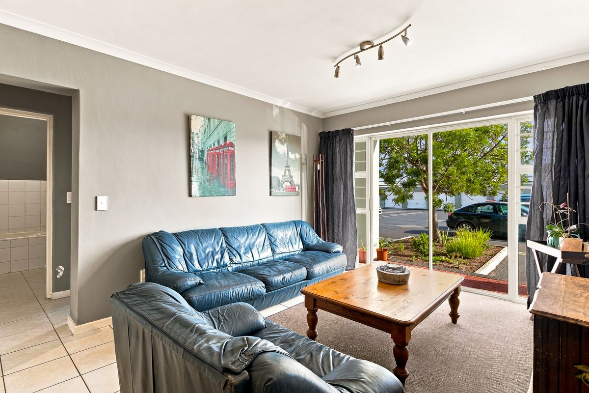 A living room featuring tiled and carpeted flooring, track lighting, and a large sliding glass door providing access to the exterior.