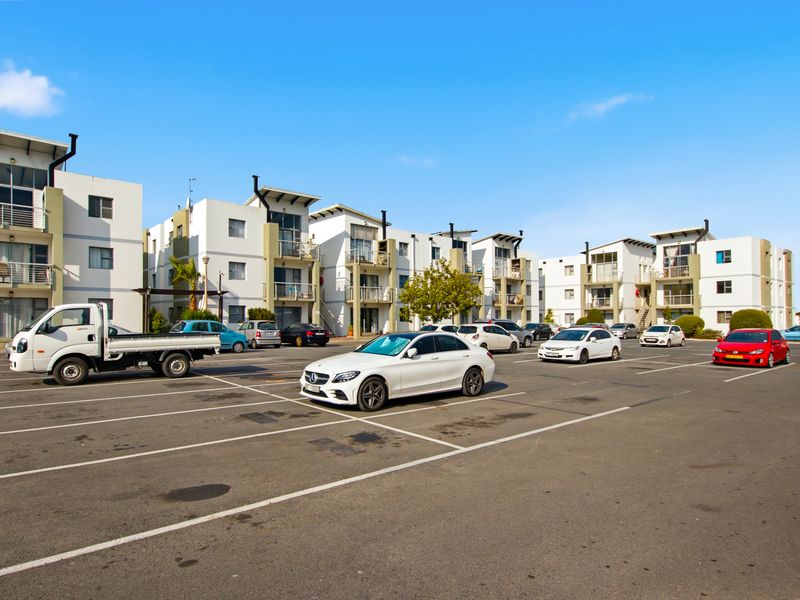 A view of the apartment complex exterior featuring a large paved parking area and multi-story residential buildings with balconies.
