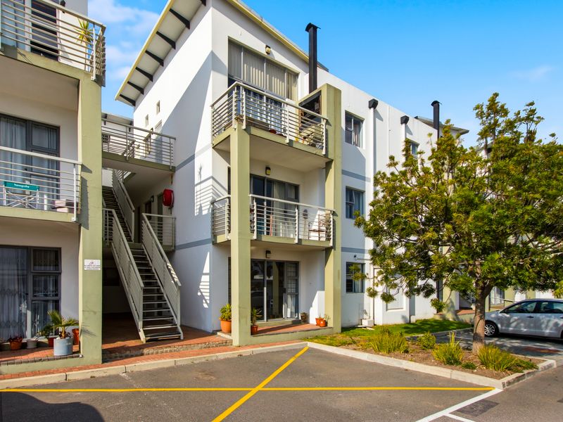 Exterior view of a multi-story apartment complex featuring private balconies, external staircases, and dedicated parking spaces.