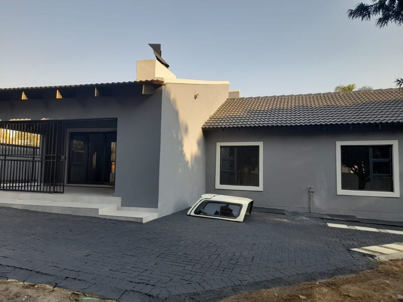 Front exterior view of a modern grey-painted house featuring a paved driveway, tiled roof, and secure gated entrance.