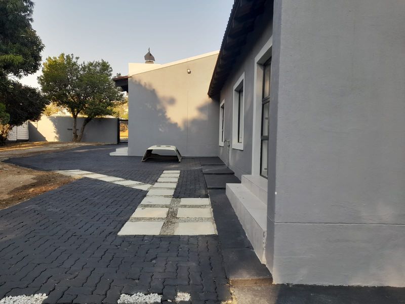 A view of the property's exterior side elevation featuring a modern grey facade, paved driveway, and concrete steps leading to the entrance.
