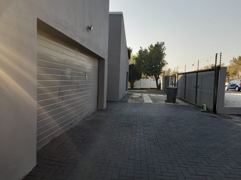 Front exterior view featuring a paved driveway, modern garage door, and secure perimeter fencing with a sliding gate.