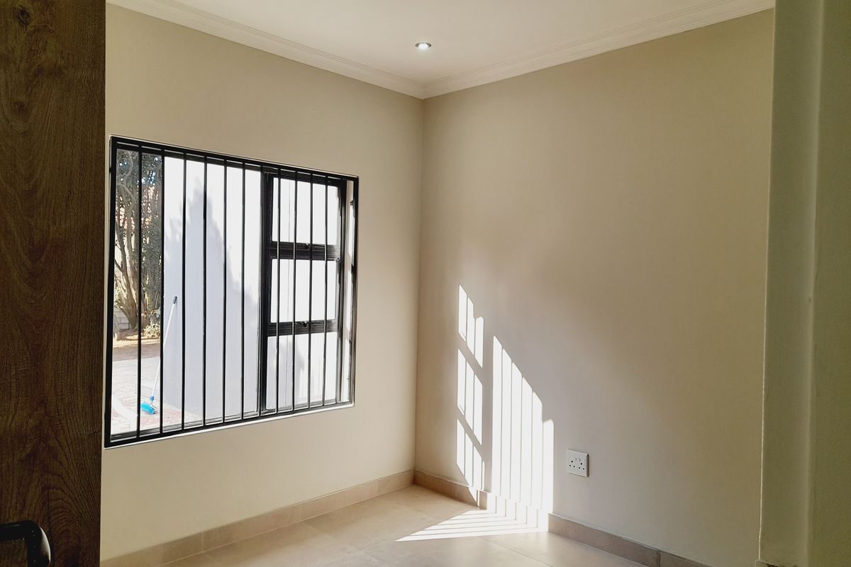 A bright, empty bedroom featuring tiled flooring, recessed downlighting, and a window fitted with security bars.