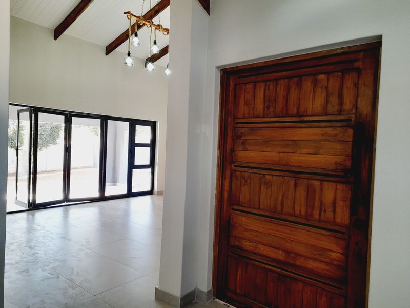 Bright entrance hall featuring high ceilings with exposed timber beams, large format floor tiles, and modern aluminium stacker doors leading to the exterior.