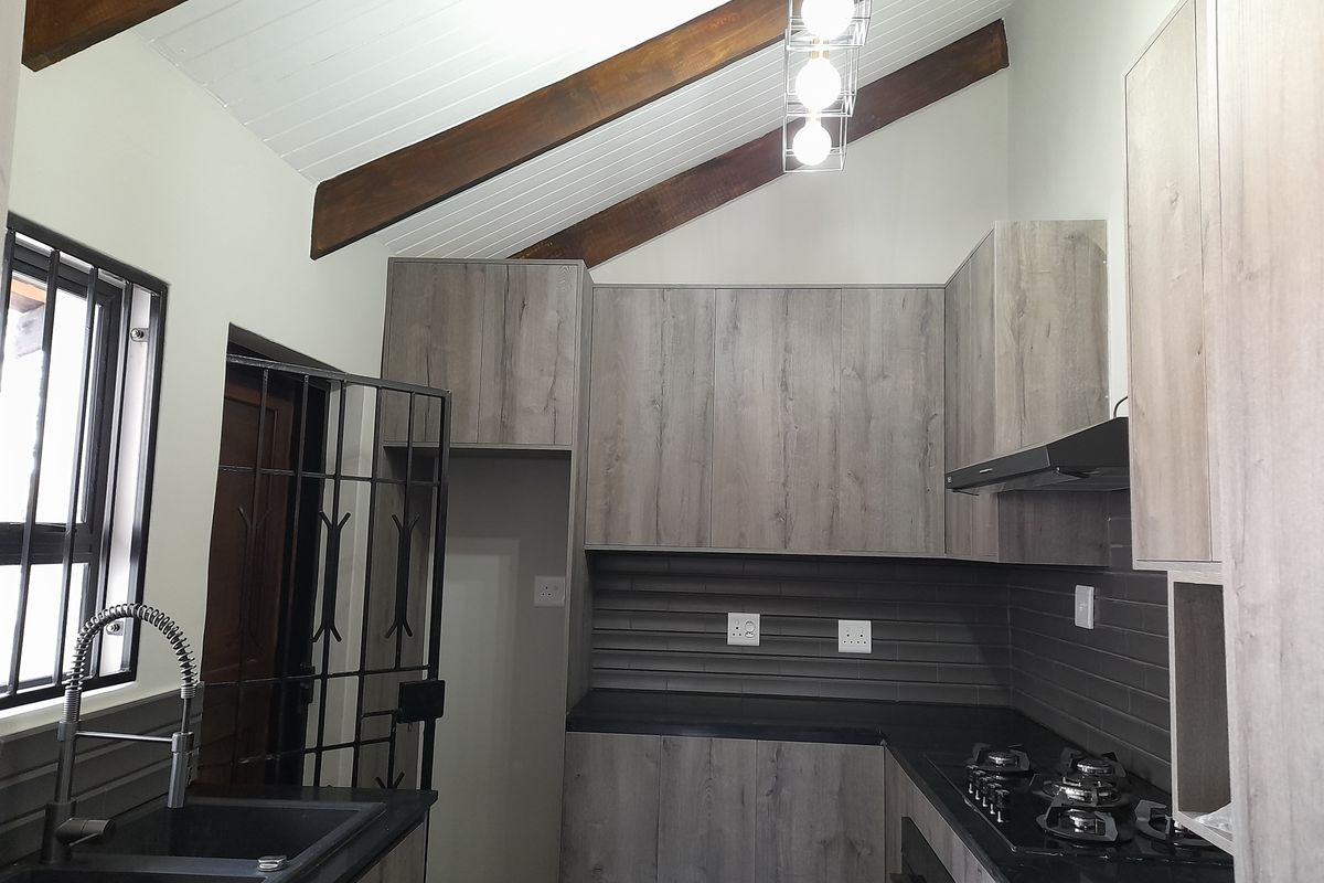 Modern kitchen featuring wood-look cabinetry, dark countertops, gas hob, extractor fan, and exposed timber beams under a vaulted ceiling.