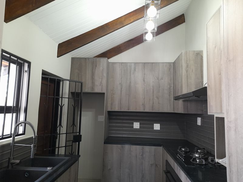 Modern kitchen featuring wood-look cabinetry, dark countertops, gas hob, extractor fan, and exposed timber beams under a vaulted ceiling.