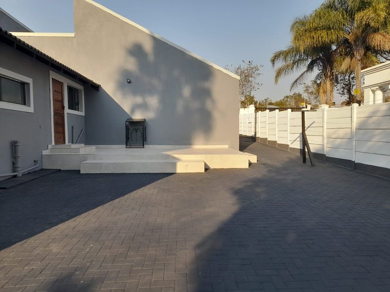 A clean rear exterior view featuring a paved driveway, concrete patio steps, and a secure precast boundary wall.