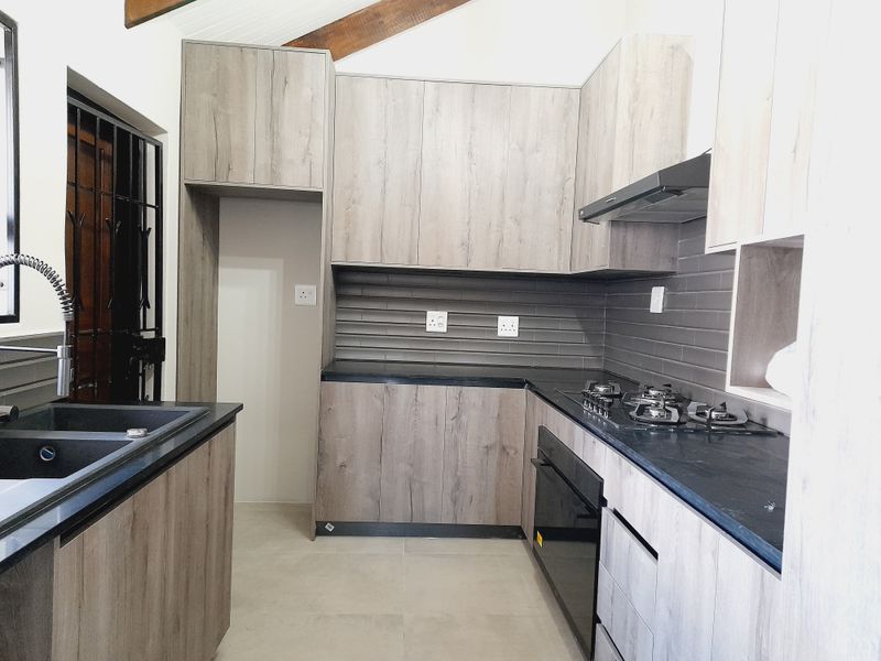 Modern kitchen featuring wood-look cabinetry, stone countertops, gas hob, built-in oven, extractor fan, and a double sink with exposed timber ceiling beams.
