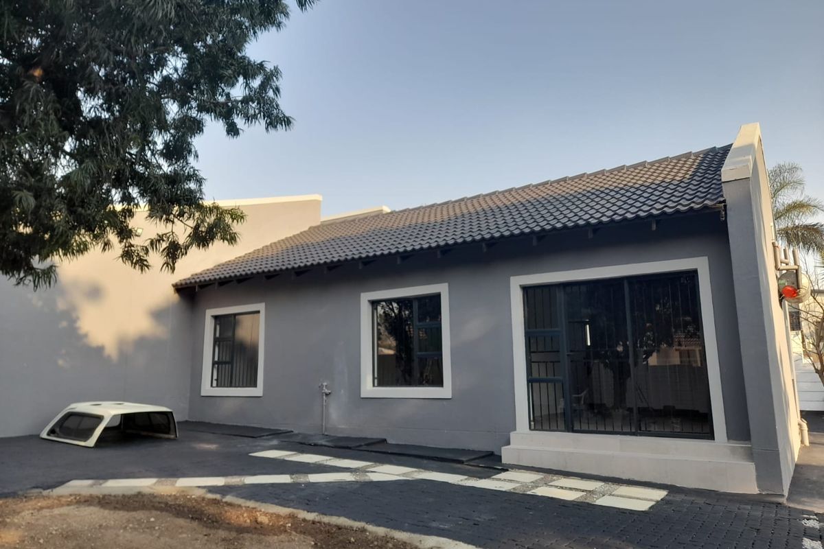 Rear exterior view of the house featuring a grey facade, tiled roof, and paved outdoor area with sliding glass doors.