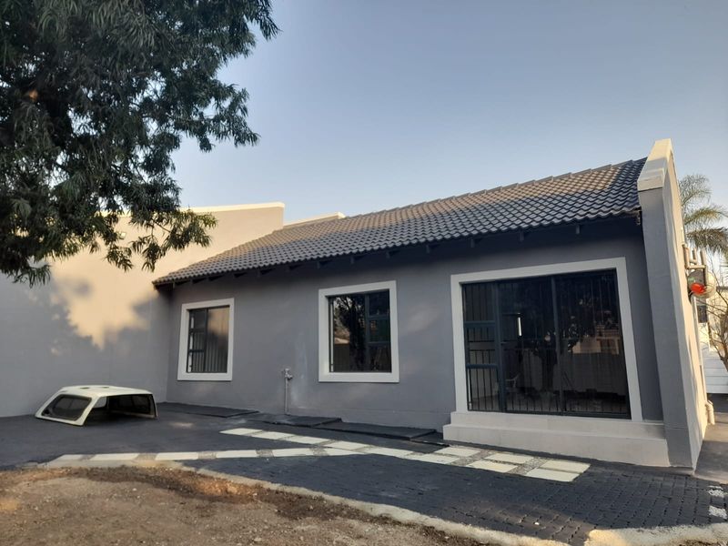 Rear exterior view of the house featuring a grey facade, tiled roof, and paved outdoor area with sliding glass doors.