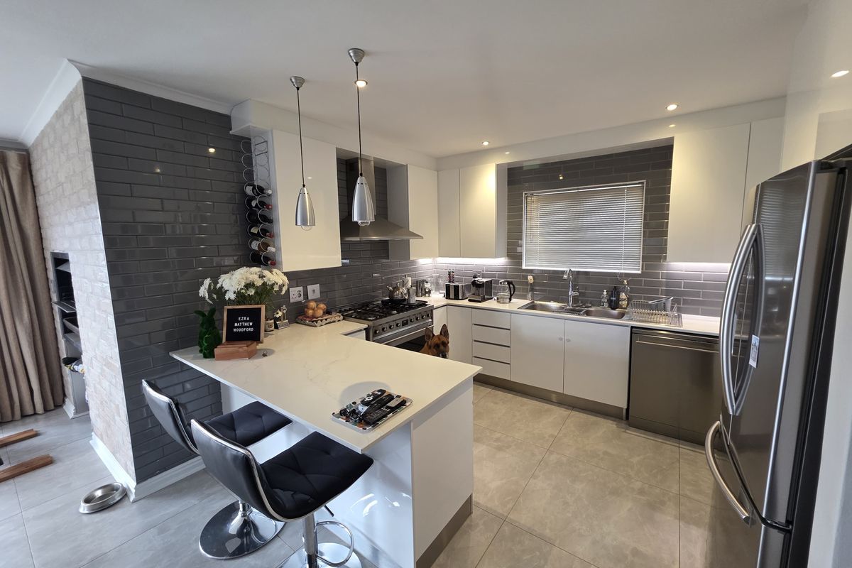 Modern kitchen featuring sleek white cabinetry, grey subway tile backsplash, quartz countertops, a breakfast bar, and high-quality stainless steel appliances.