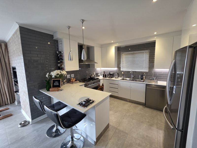 Modern kitchen featuring sleek white cabinetry, grey subway tile backsplash, quartz countertops, a breakfast bar, and high-quality stainless steel appliances.