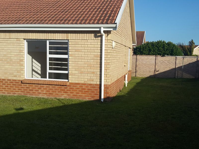 Rear view of the townhouse featuring a brick facade, tiled roof, aluminium windows, and a private grassed garden enclosed by a brick boundary wall.