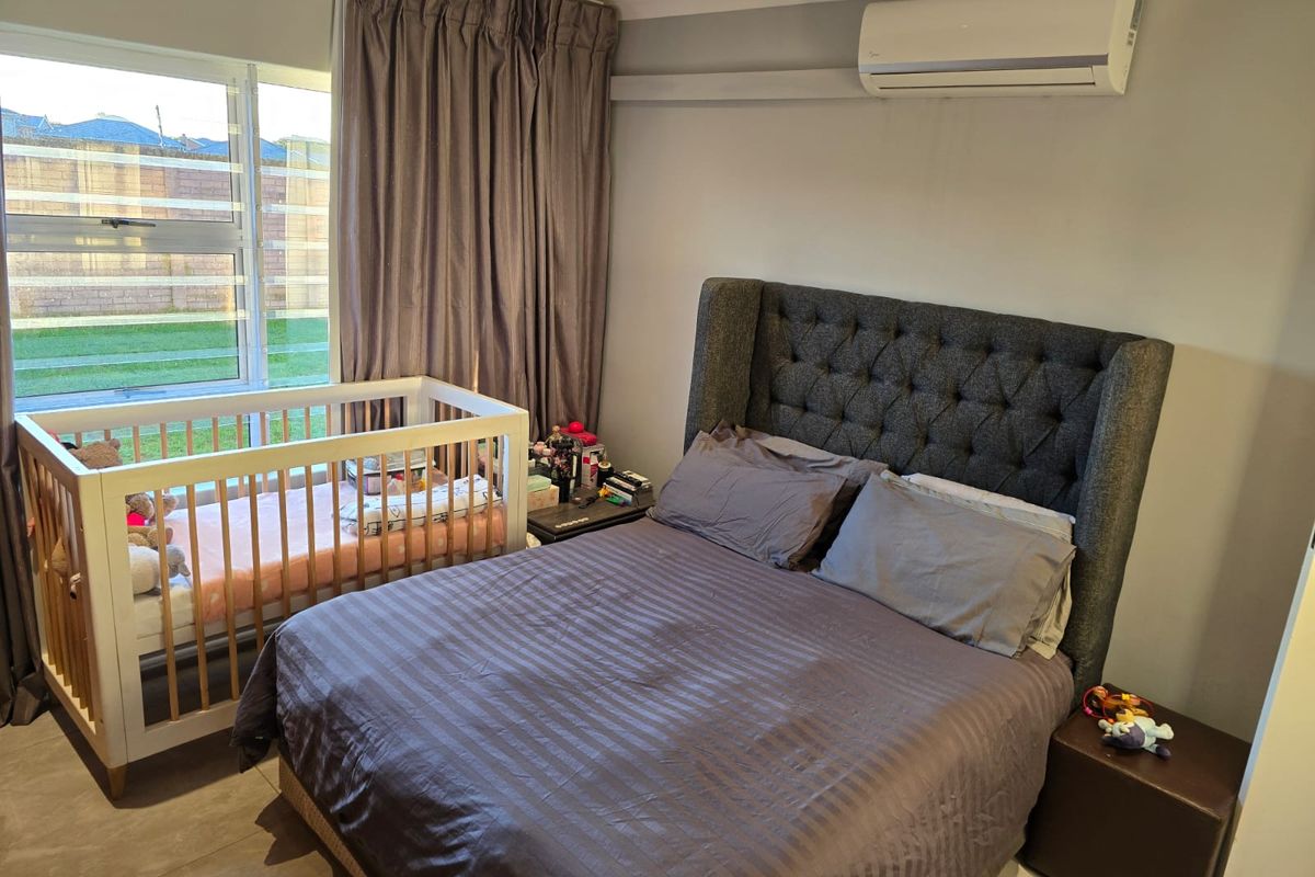 A well-maintained bedroom featuring tiled flooring, recessed downlighting, and a wall-mounted air conditioning unit, with large windows providing natural light.