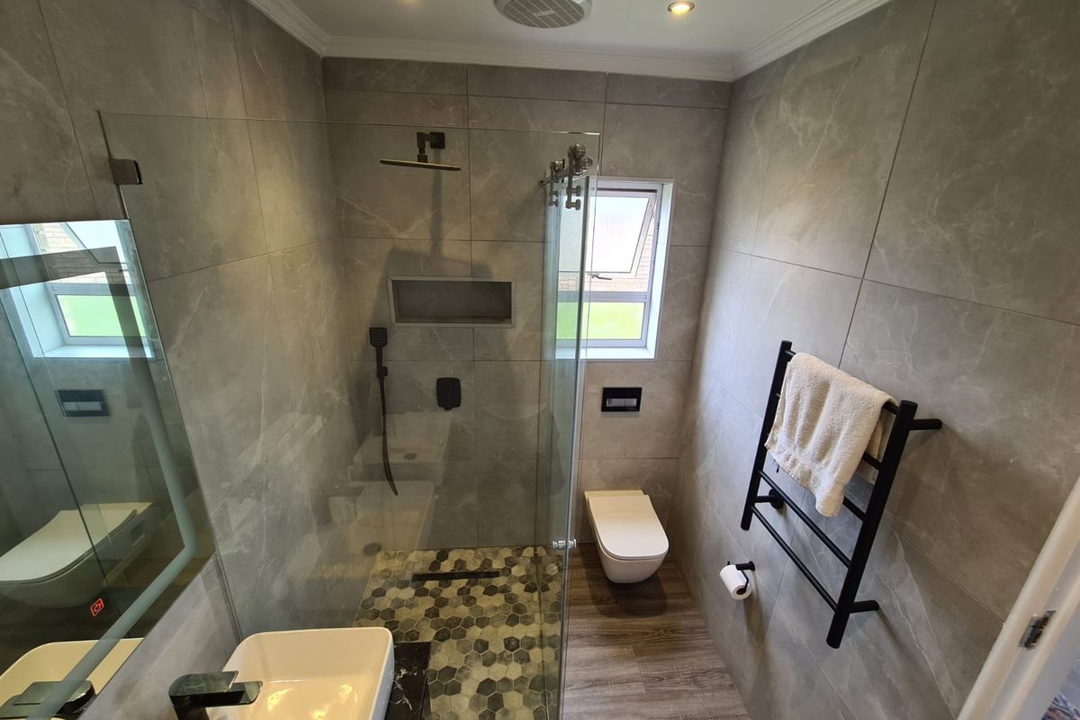 Modern bathroom featuring a walk-in shower with mosaic floor tiles, wall-hung toilet, heated towel rail, and contemporary grey wall tiling.