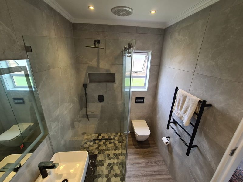 Modern bathroom featuring a walk-in shower with mosaic floor tiles, wall-hung toilet, heated towel rail, and contemporary grey wall tiling.