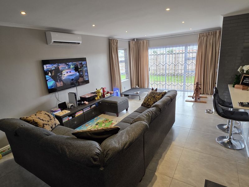 Spacious open-plan living area featuring tiled floors, recessed lighting, a split-system air conditioner, and a brick feature wall with access to the rear garden.