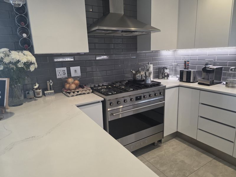 Modern kitchen featuring white cabinetry, quartz countertops, subway tile backsplash, and a high-end Smeg gas stove with stainless steel extractor.