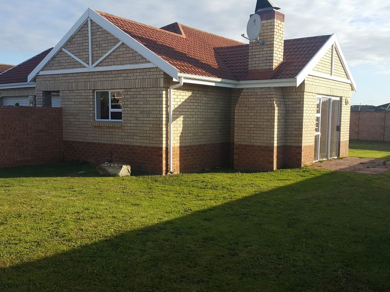 Rear view of a face-brick townhouse featuring a tiled roof, chimney, sliding glass doors, and a private garden with a paved patio area.