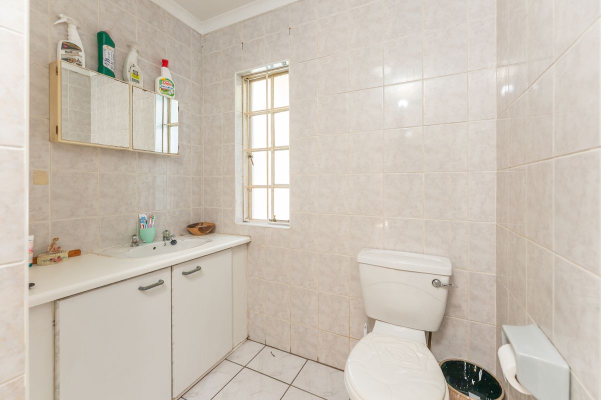 A dated bathroom featuring tiled walls and floors, a vanity cabinet with a basin, and a standard toilet.