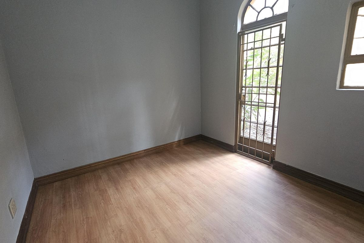 An empty bedroom featuring light wood-look laminate flooring, neutral walls, and a secure arched door leading to the exterior.