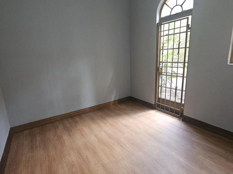 An empty bedroom featuring light wood-look laminate flooring, neutral walls, and a secure arched door leading to the exterior.