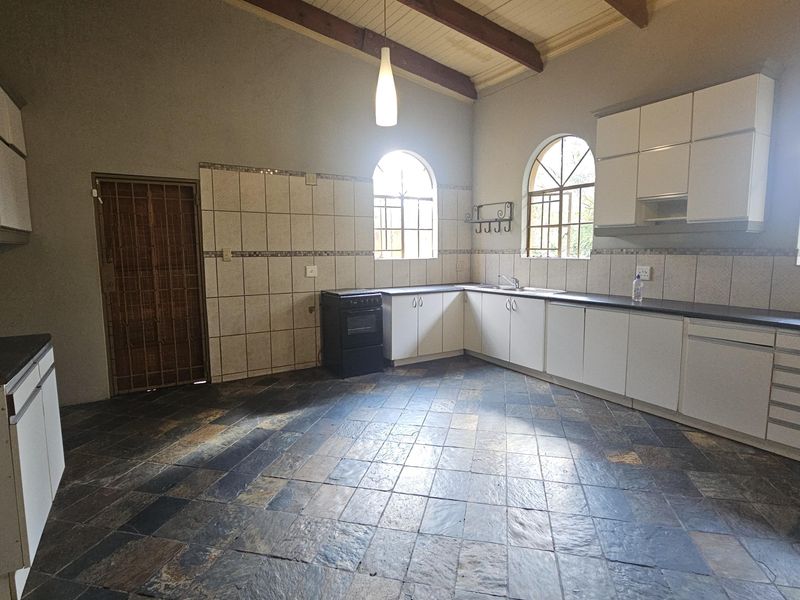 Spacious kitchen featuring slate tile flooring, exposed timber ceiling beams, arched windows, and ample built-in cabinetry with a tiled backsplash.