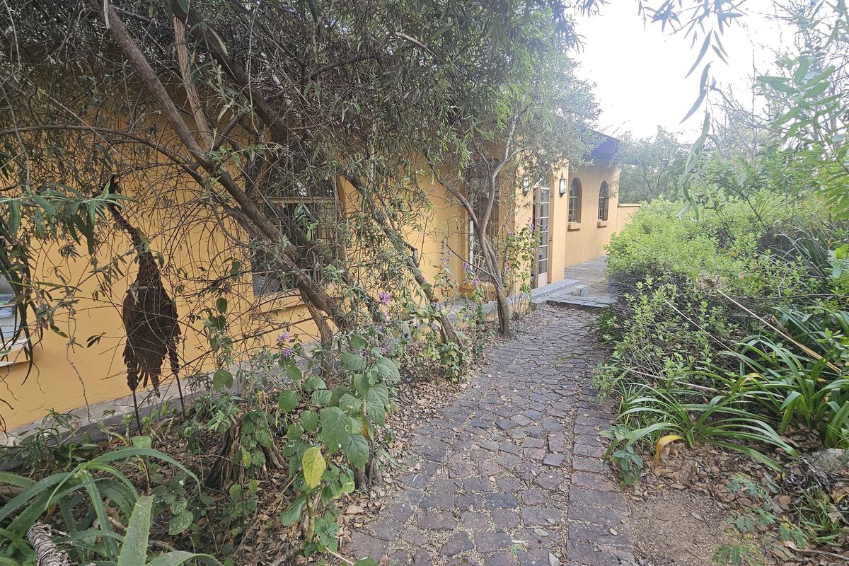 A rear exterior view of the property featuring a cobblestone pathway leading along the side of the house with mature garden landscaping.