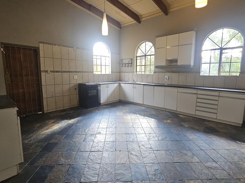 Spacious kitchen featuring slate flooring, exposed timber beams, arched windows, and ample built-in cabinetry with a functional layout.