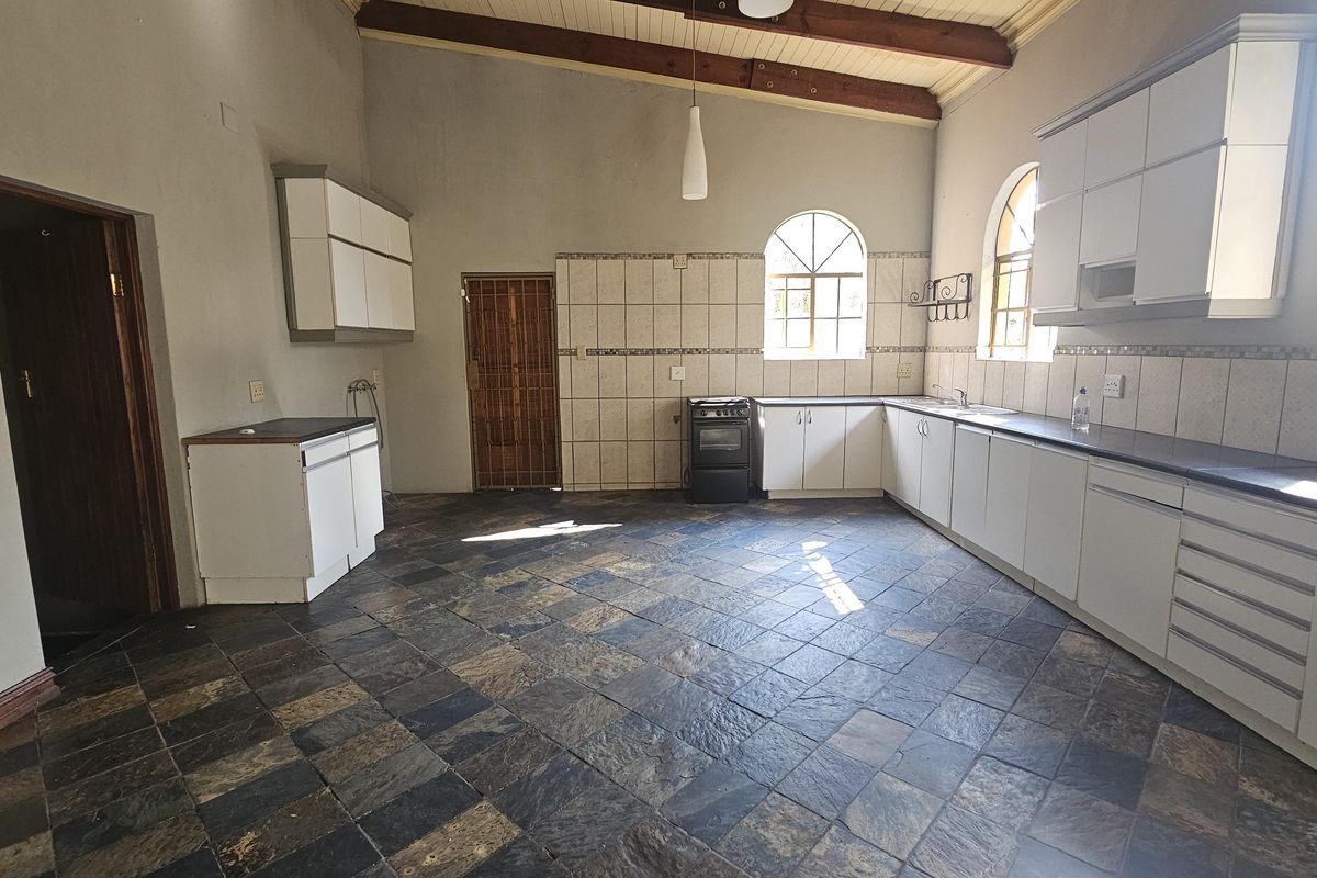 Spacious kitchen featuring exposed timber ceiling beams, arched windows, stone tile flooring, and ample built-in cabinetry with a tiled splashback.