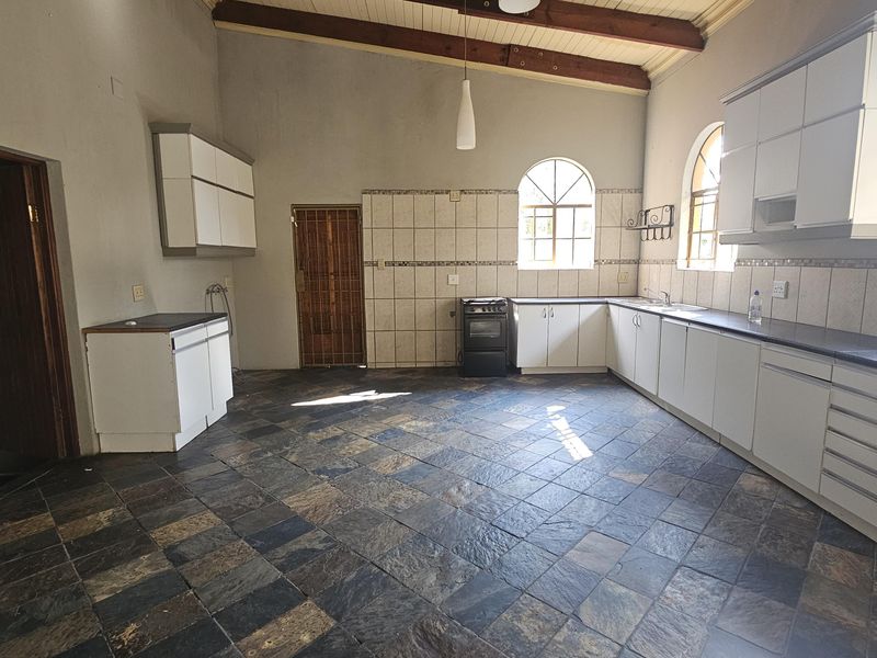 Spacious kitchen featuring exposed timber ceiling beams, arched windows, stone tile flooring, and ample built-in cabinetry with a tiled splashback.