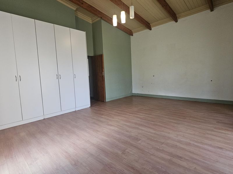 Spacious bedroom featuring laminate flooring, built-in cupboards, and an attractive vaulted ceiling with exposed timber beams.