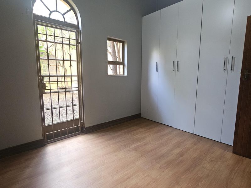 A bright, empty bedroom featuring laminate flooring, built-in cupboards, and a secure arched door leading to the exterior.