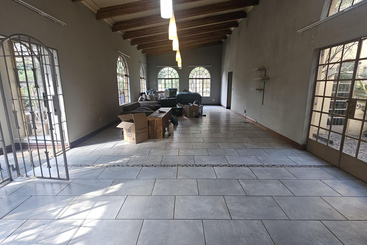 Spacious living area featuring exposed timber ceiling beams, large arched windows, and neutral tiled flooring with direct access to outdoor areas via security-fitted doors.