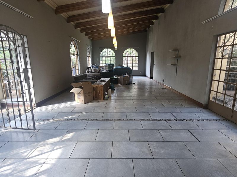 Spacious living area featuring exposed timber ceiling beams, large arched windows, and neutral tiled flooring with direct access to outdoor areas via security-fitted doors.