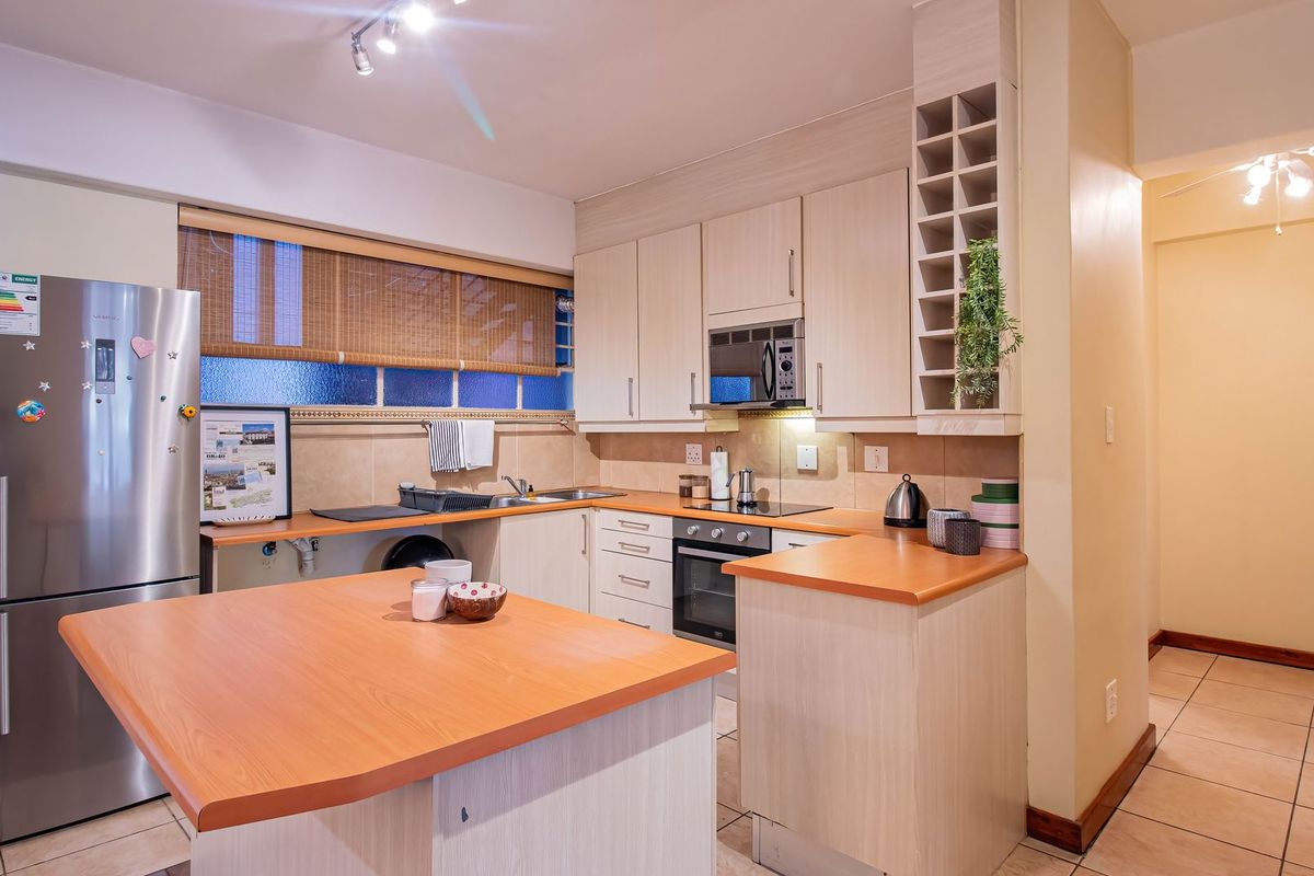 A functional kitchen featuring light wood-finish cabinetry, laminate countertops, built-in oven, hob, and microwave, with tiled flooring and backsplash.