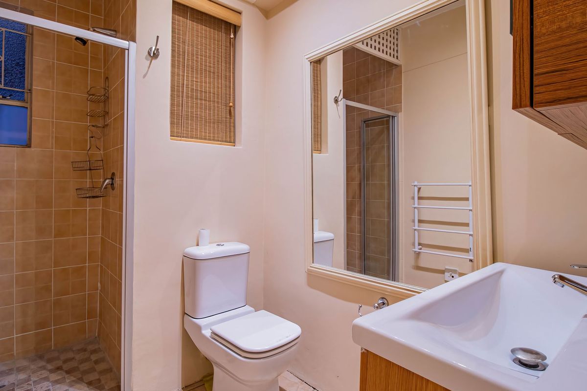 A clean and functional bathroom featuring a shower enclosure, vanity basin, wall-mounted mirror, and a heated towel rail.