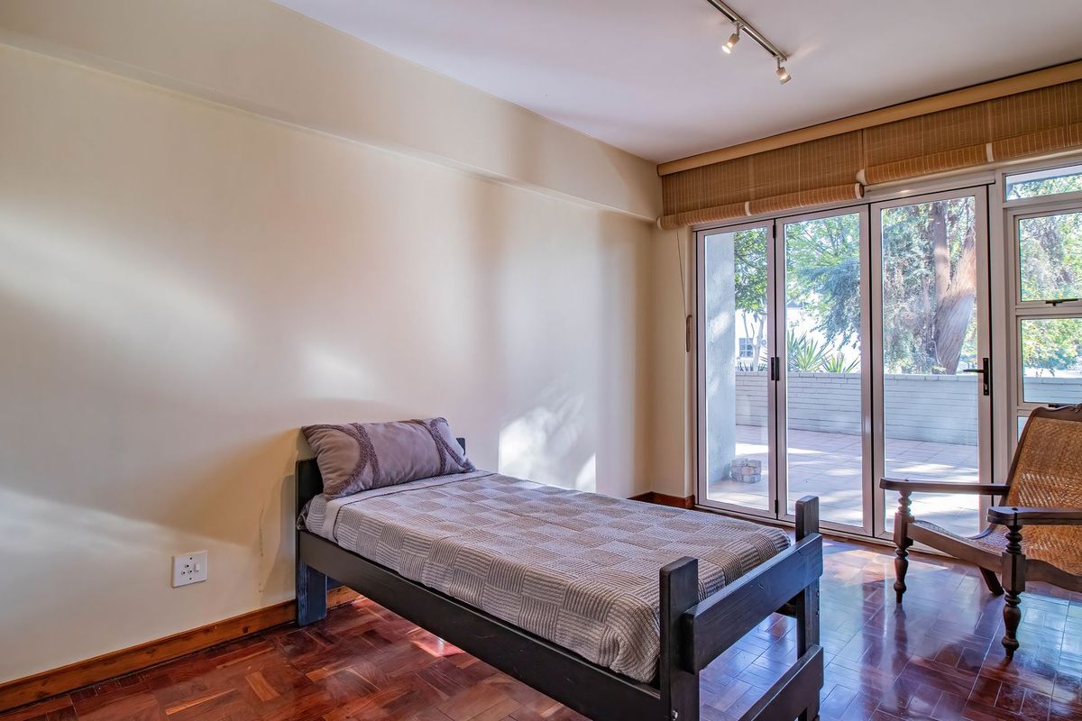 A bedroom featuring polished parquet flooring, track lighting, and large sliding glass doors that provide access to an outdoor patio area.