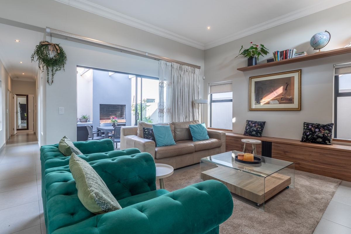 A bright and spacious living room featuring tiled floors, recessed lighting, and built-in wooden shelving, with seamless access to an outdoor patio area.