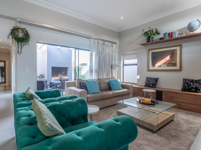 A bright and spacious living room featuring tiled floors, recessed lighting, and built-in wooden shelving, with seamless access to an outdoor patio area.