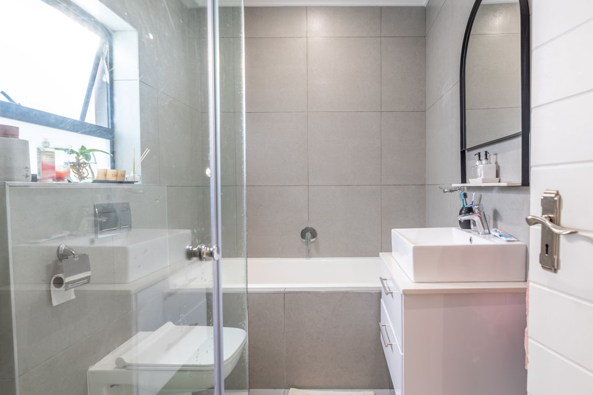 Modern bathroom featuring a glass-enclosed shower, built-in bathtub, wall-mounted toilet, and a sleek vanity with a vessel sink and arched mirror.