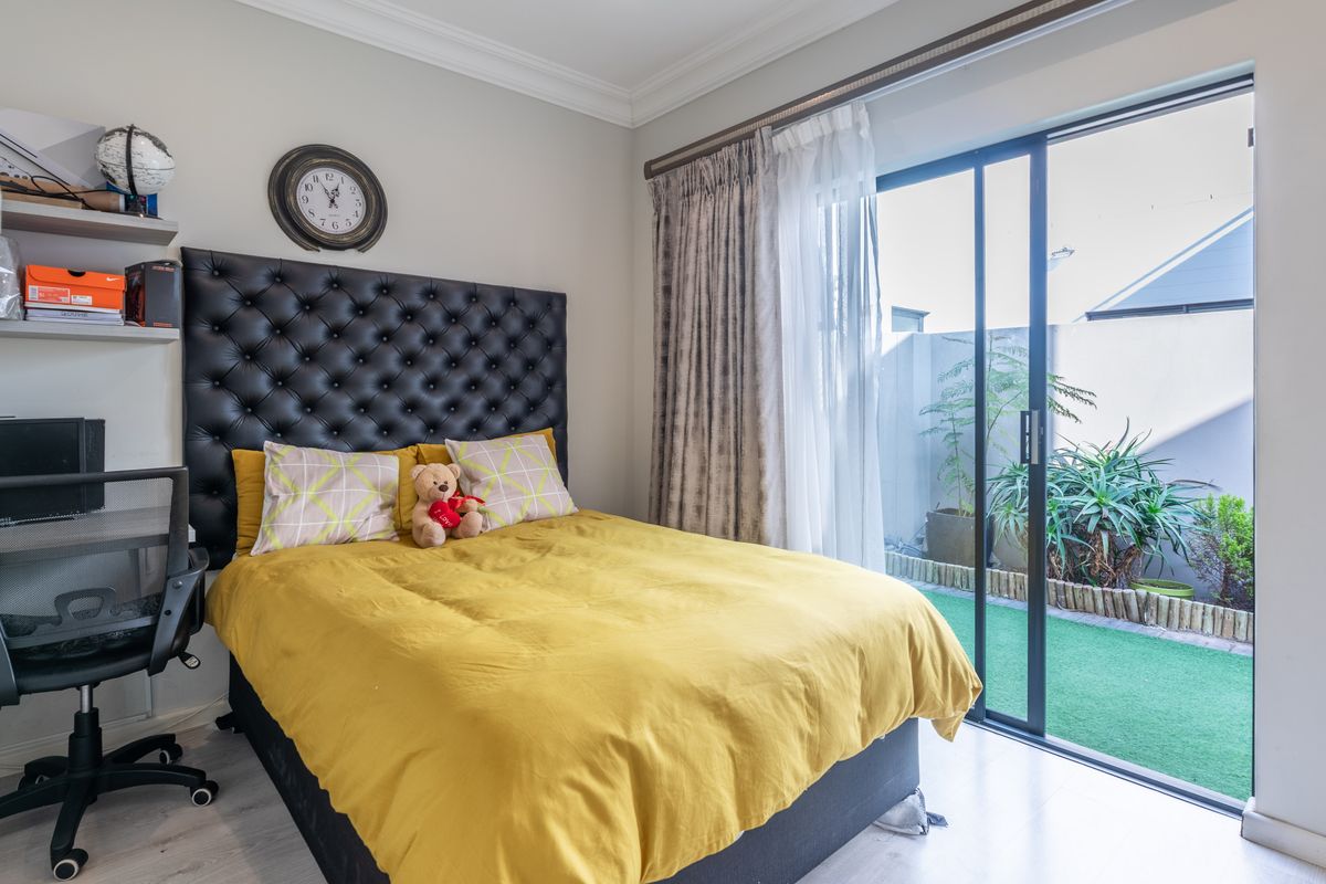 A well-maintained bedroom featuring crown molding, laminate flooring, and a large sliding glass door providing direct access to a private outdoor garden area.