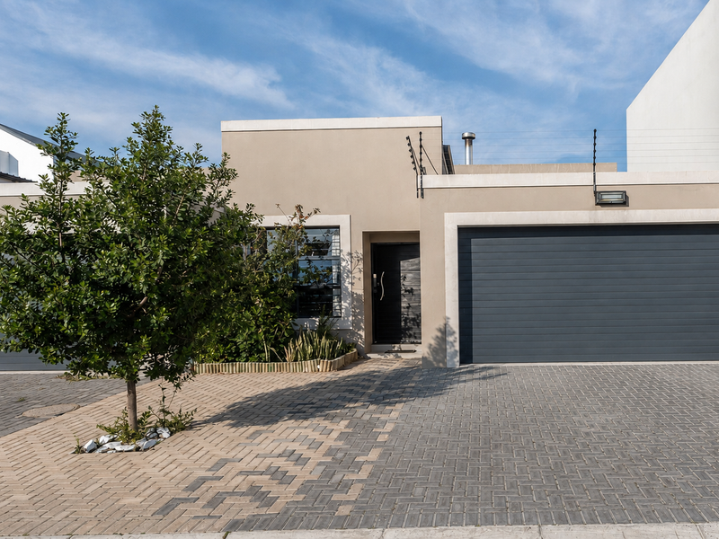 Modern front elevation featuring a double garage, paved driveway, and secure electric fencing, presenting a clean and well-maintained contemporary facade.
