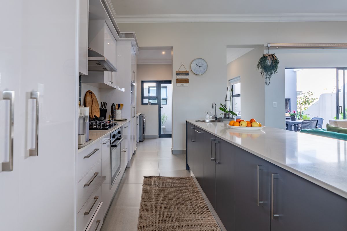 Modern kitchen featuring a large central island with stone countertops, high-gloss cabinetry, integrated appliances, and a seamless flow into the adjacent living area.