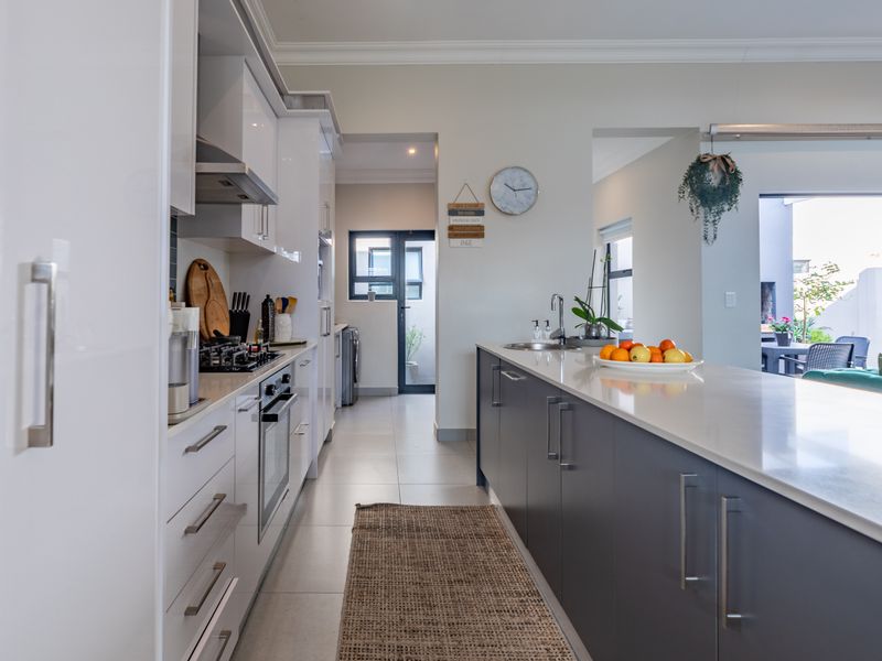 Modern kitchen featuring a large central island with stone countertops, high-gloss cabinetry, integrated appliances, and a seamless flow into the adjacent living area.
