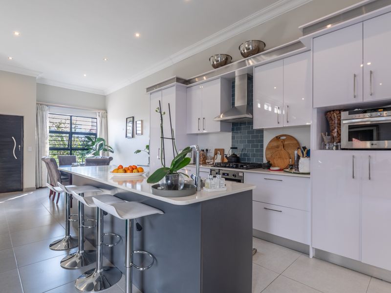 Modern open-plan kitchen featuring a central island with breakfast bar, high-gloss cabinetry, integrated appliances, and sleek tiled flooring throughout the living space.