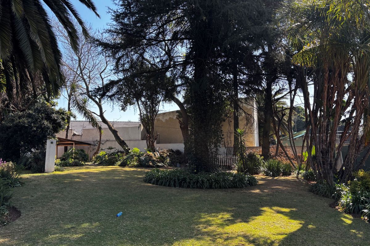 A spacious, well-established garden featuring mature trees, lush greenery, and a boundary wall, offering a private and tranquil outdoor setting.