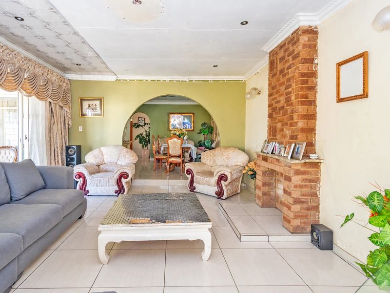 Open-plan living and dining area featuring a prominent exposed brick fireplace, tiled flooring, and a decorative archway connecting the two spaces.